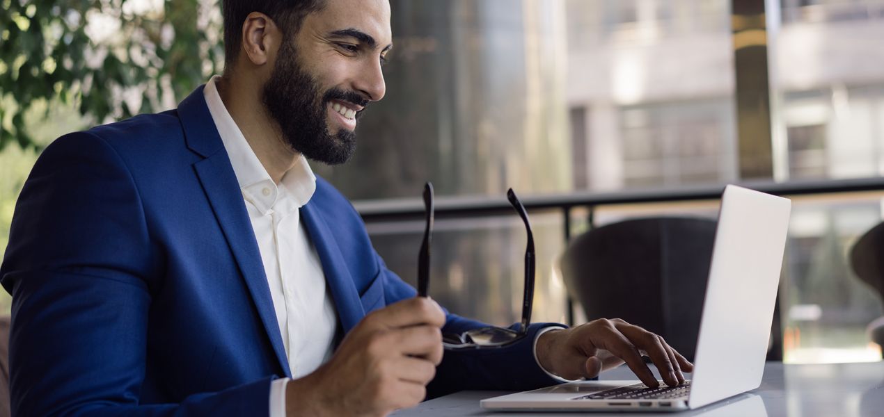 A suited man is seated at a table, working intently on his laptop